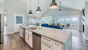 A spacious kitchen with a large island, modern pendant lights, and a view of the ocean through large sliding doors.