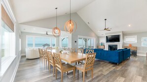 A spacious living area with a large wooden dining table, blue sofa, and a TV mounted on the wall.