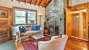A cozy living room with a stone fireplace, wooden beams, and a large window. - Wawayanda House on 62 Acres - Multiple Fireplaces! (Middletown)