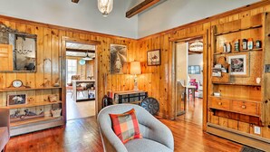 A spacious room with wooden paneling, a grey armchair with a plaid cushion, a vintage clock, and a chandelier. - Wawayanda House on 62 Acres - Multiple Fireplaces! (Middletown)