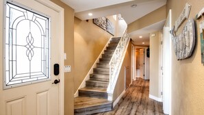 Un pasillo con escalera de madera, paredes color crema y una puerta de cristal decorativa.