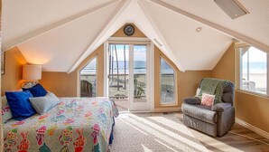 Un dormitorio con una cama grande, una silla y vista a la playa a través de un ventanal corredera.
