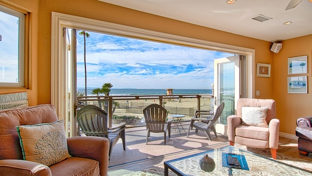 Una habitación con una mesa de vidrio, dos sillas, un sofá y vista a la playa y al océano.