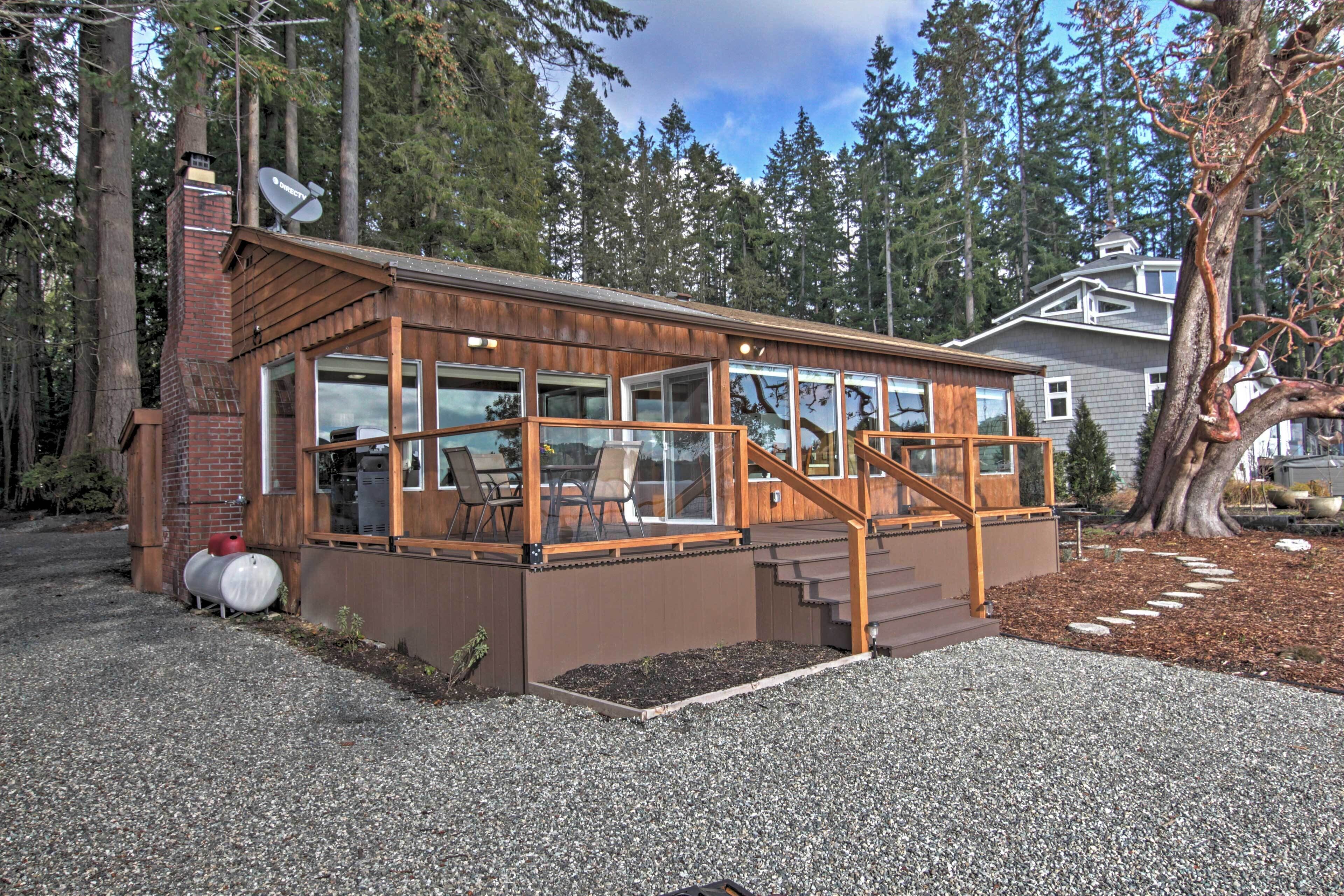 A modern cabin with a large glass window section, a wooden deck, and a gravel driveway.