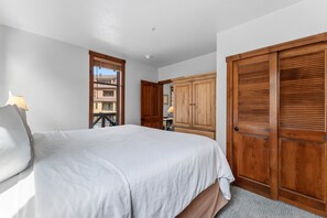 A bedroom with a large bed, wooden wardrobe, and a window with blinds.