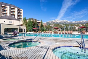 A pool area with hot tubs, lounge chairs, and a mountain view.