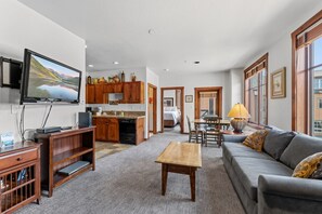 A modern living room with a flat-screen TV, wooden furniture, a sofa, and a dining area with a table and chairs.