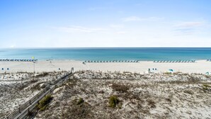 A beach with a wooden boardwalk leading to the water, sandy dunes, and a clear blue sky.