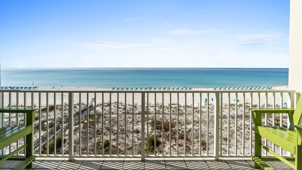 A balcony with a view of the beach, a railing, and a green bench.