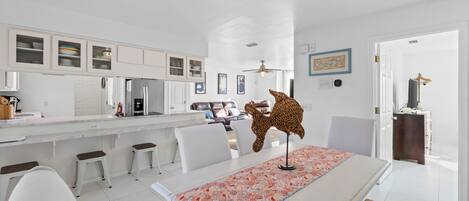 A modern kitchen with white cabinetry, a central island, and a dining area with a table and chairs.