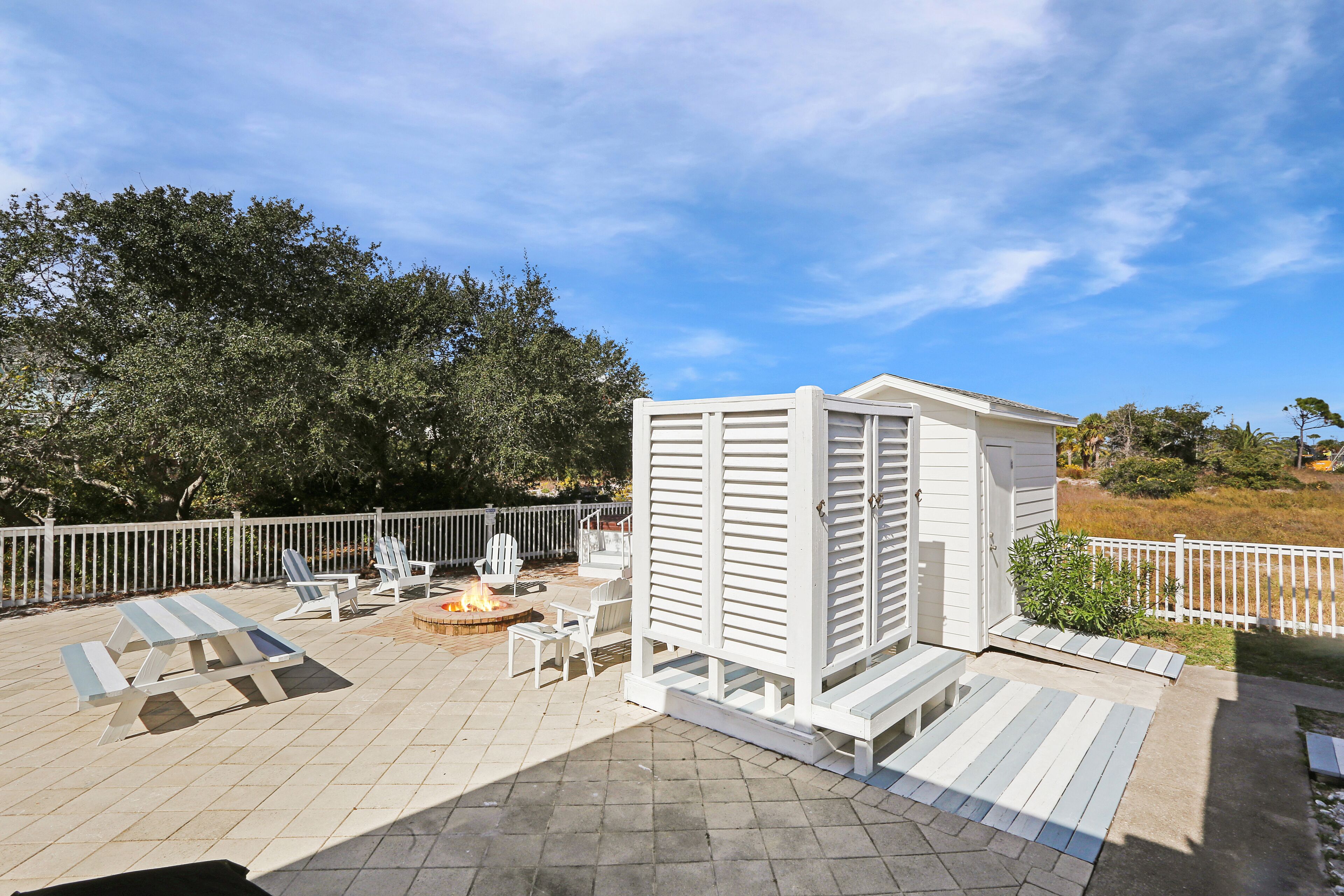 Un patio con mobiliario exterior, un cobertizo blanco pequeño y un pozo de fuego.