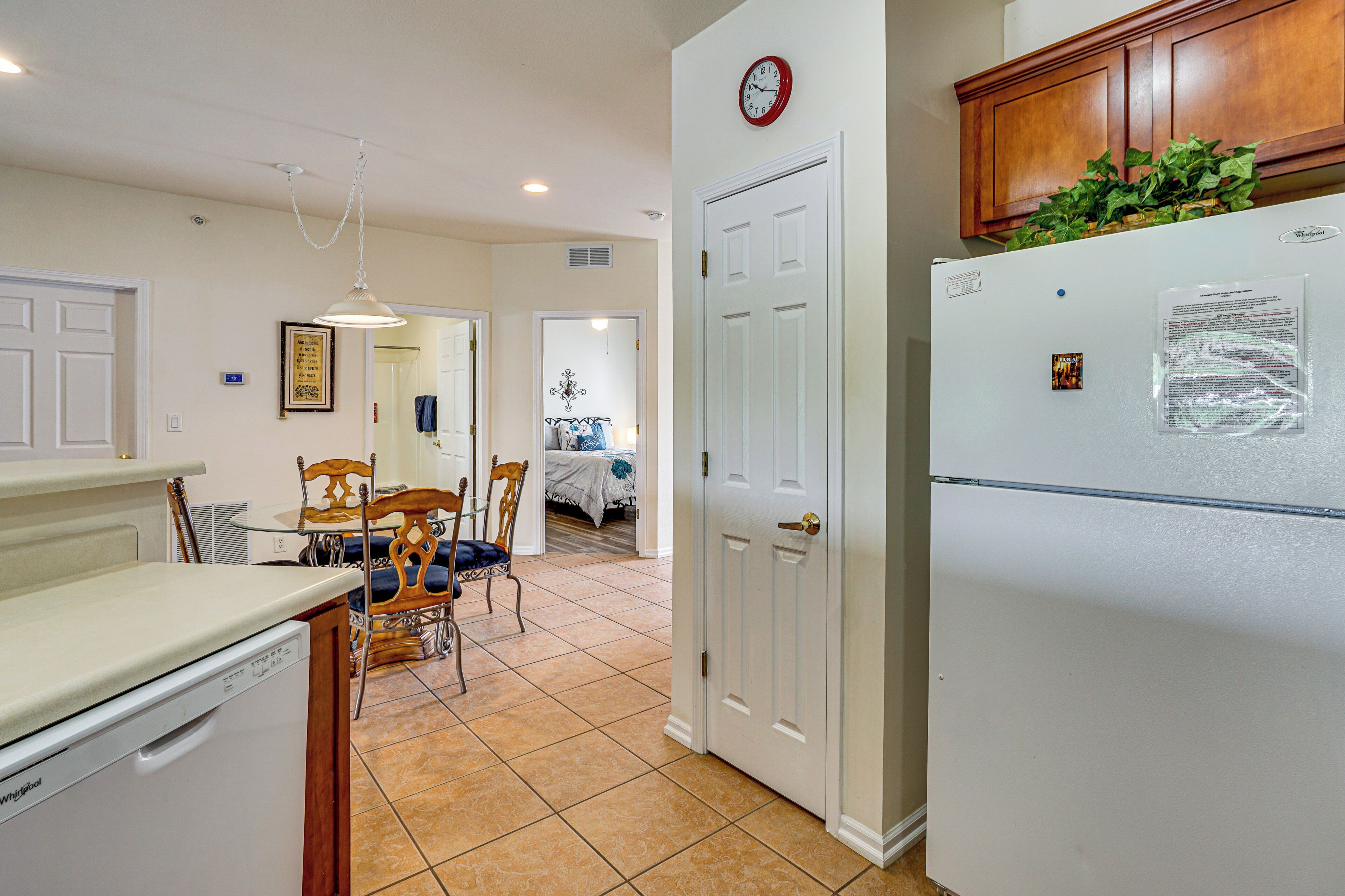 A kitchen with a refrigerator, a dining table with chairs, and a clock on the wall.