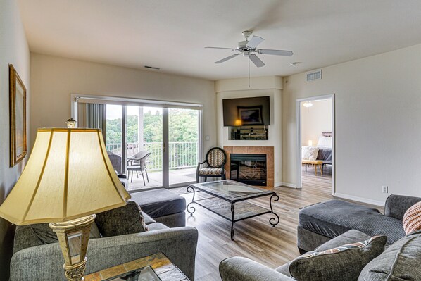 A living room with a glass coffee table, sofas, a lamp, a fireplace, and a ceiling fan.