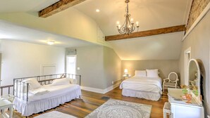 A spacious bedroom with two beds, a chandelier, a vanity with a mirror, and a wooden ceiling beam. - Historic Ottawa Lake House: Deck, Barn + 96 Acres! (Ottawa Lake)