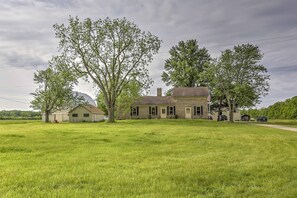 A two-story house with a brick exterior, surrounded by a large grassy field and trees. - Historic Ottawa Lake House: Deck, Barn + 96 Acres! (Ottawa Lake)