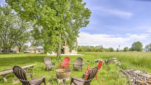 An outdoor seating area with Adirondack chairs and a fire pit, surrounded by a grassy field and trees. - Historic Ottawa Lake House: Deck, Barn + 96 Acres! (Ottawa Lake)