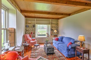 A cozy living room with a blue sofa, red armchair, and a wooden ceiling. - Historic Ottawa Lake House: Deck, Barn + 96 Acres! (Ottawa Lake)