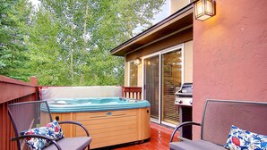 Una terraza de madera con un jacuzzi, dos sillas con cojines y una parrilla para barbacoa.