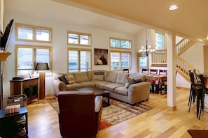 A spacious living room with a large sectional sofa, a coffee table, and a fireplace. There are multiple windows providing natural light, and a staircase leading to an upper level. - Private HotTub-Steps 2Mtn/Town Bus-Garage-Grill (Steamboat Springs)