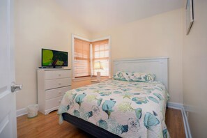 A bedroom with a bed, a nightstand, a television, and a window with blinds.