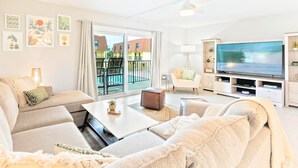 Ein modernes Wohnzimmer mit Sofa, Couchtisch, Fernseher und Balkon mit Blick auf einen Pool.