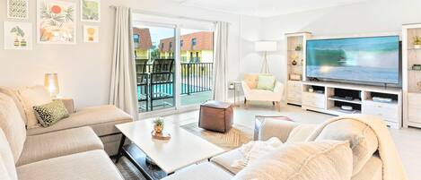 A modern living room with a sofa, a coffee table, a TV, and a balcony with a pool view.