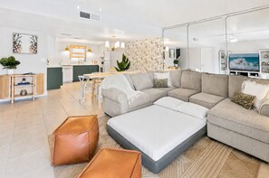 Un salon moderne avec un canapé d’angle, des poufs et un coin repas comprenant une table et des chaises.