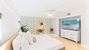 Ein Schlafzimmer mit einem Bett, einem Schreibtisch, einem Stuhl, einem Fernseher und einem Deckenventilator.