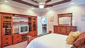 Ein Schlafzimmer mit einem Bett, Holzmöbeln, einem Deckenventilator und einem Fernseher.