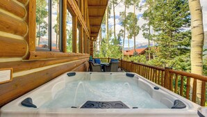 Eine Holzhütte mit Whirlpool auf einer Terrasse, mit Blick auf eine gebirgige Landschaft.