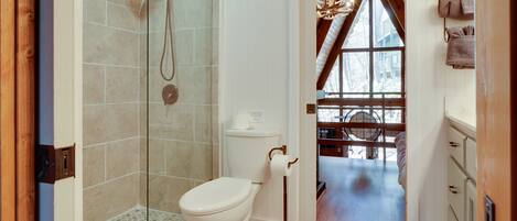 Un baño con ducha acristalada, inodoro y soporte para papel higiénico a la vista.