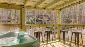 Een bubbelbadgedeelte met een houten terras, metalen krukken en uitzicht op een bebost gebied door grote ramen.