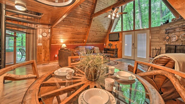 Een ruime houten hut met een eethoek, inclusief een glazen tafel, houten stoelen en een kroonluchter.