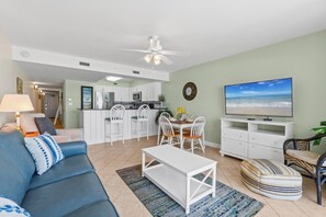 A living room with a sofa, coffee table, TV, and dining area with chairs and a table.
