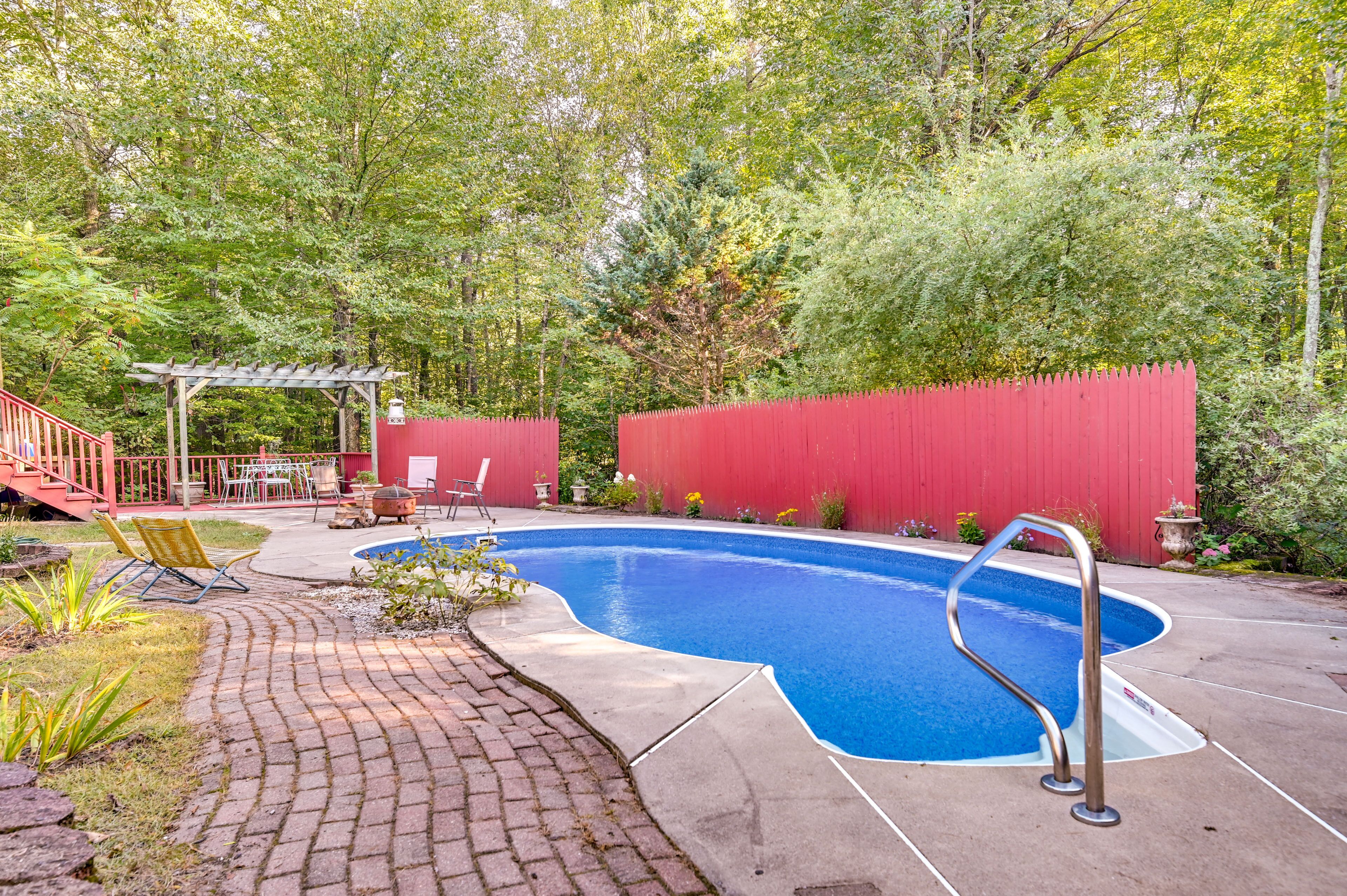A backyard with a swimming pool, a red fence, and a pergola.