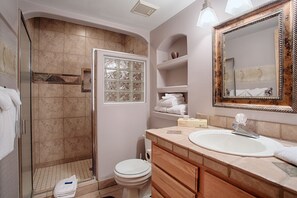 A modern bathroom with a glass shower enclosure, a toilet, a vanity with a sink, and a mirror with a decorative frame.