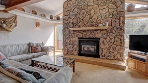 Una sala de estar con chimenea de piedra, un sofá, una mesa de centro de vidrio y una televisión.