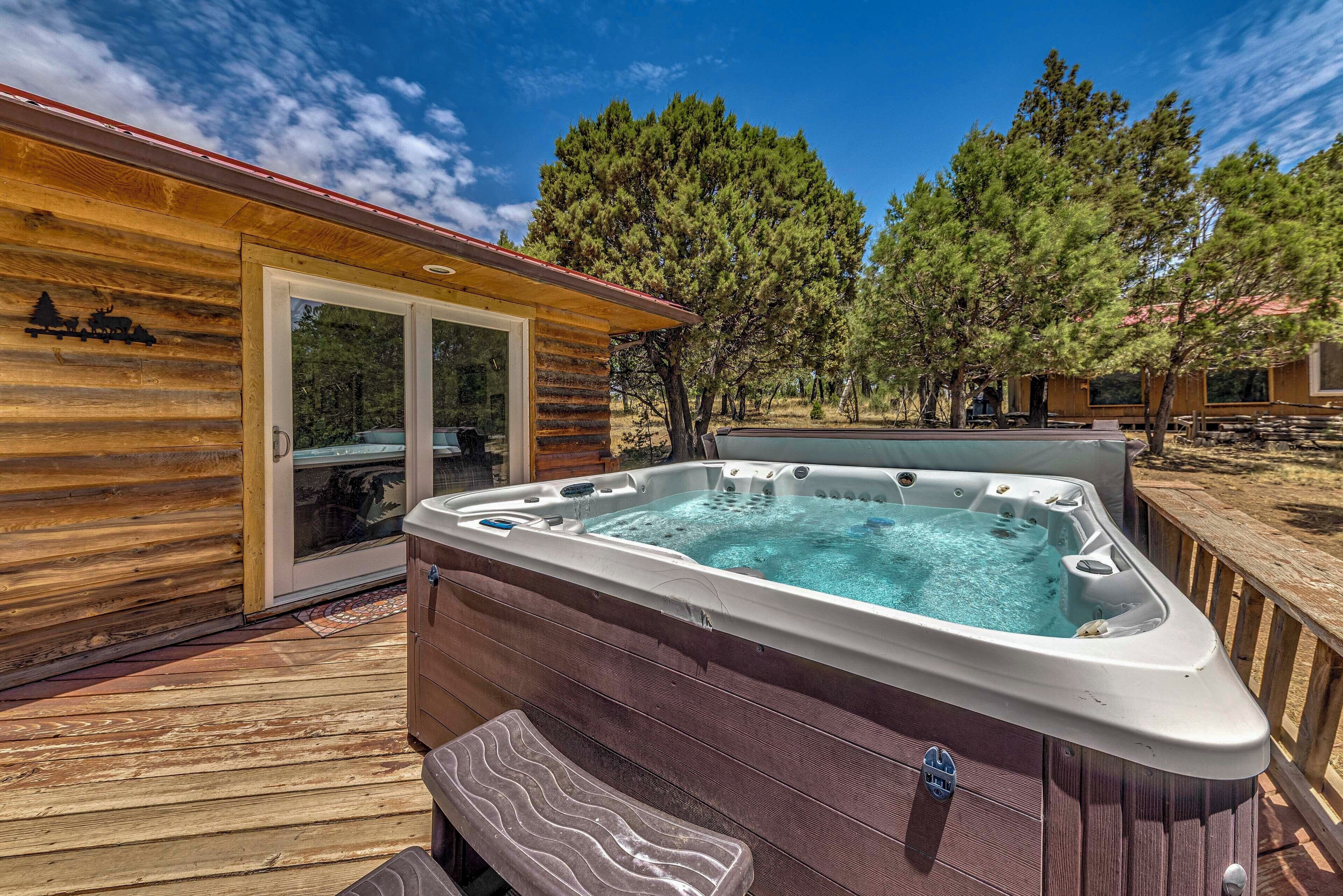 Una cabaña de madera con un jacuzzi en una terraza, rodeada de árboles.