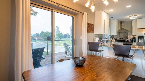 Une cuisine moderne dotée d’un grand îlot central, d’un coin repas avec une table en bois et d’une vue sur une terrasse extérieure, accessible par une porte-fenêtre coulissante.
