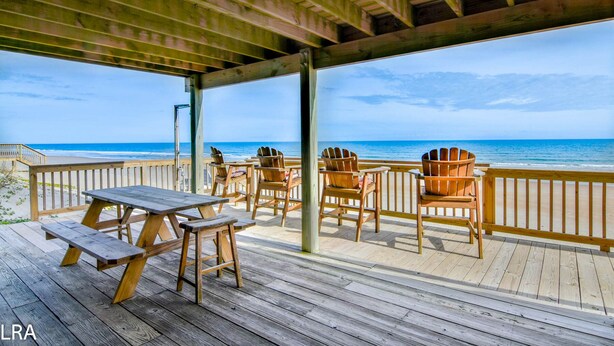 Um deck de madeira com mesa e cadeiras, com vista para a praia.