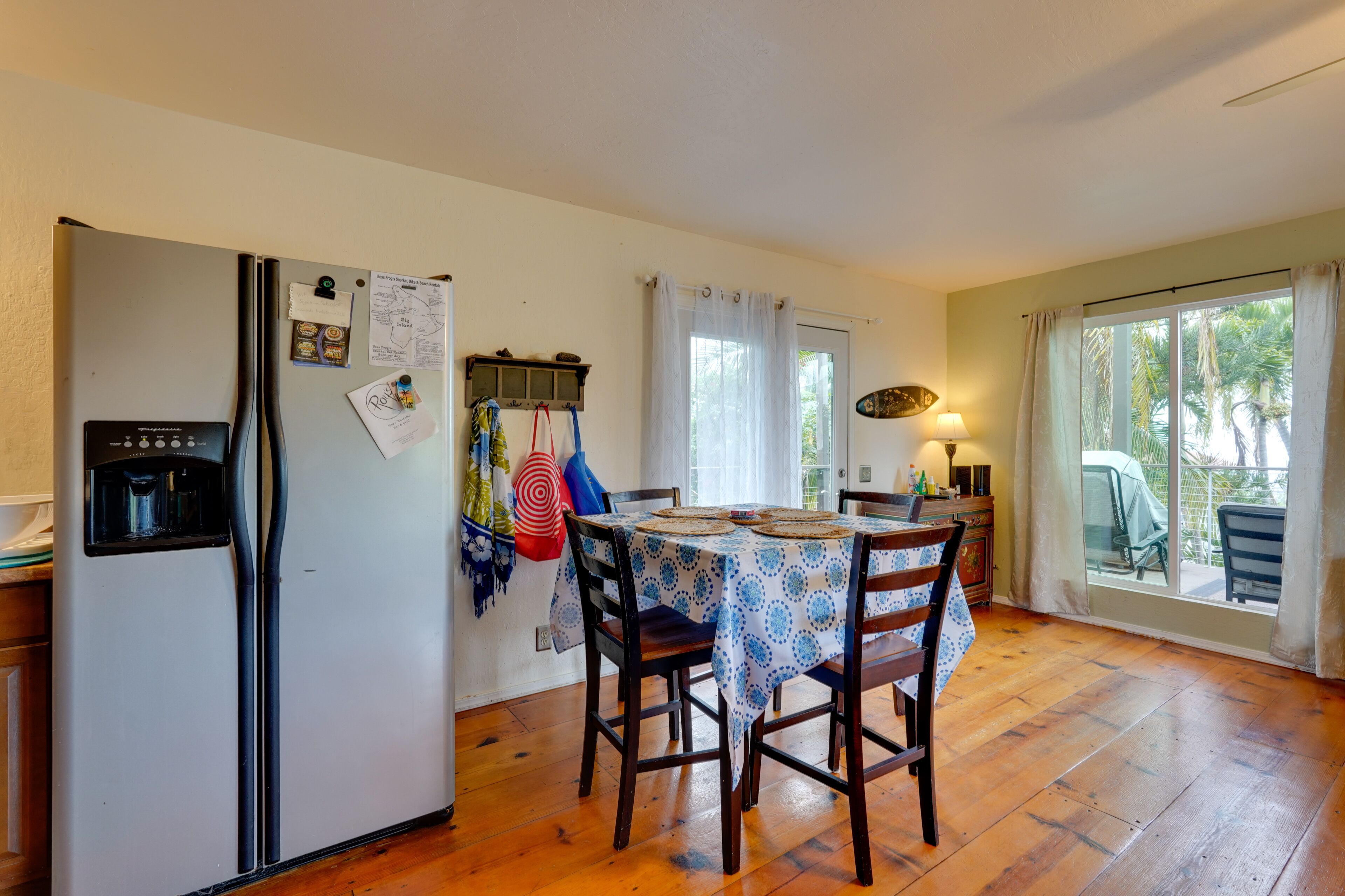 A kitchen with a refrigerator, a table with chairs, and a window with curtains.