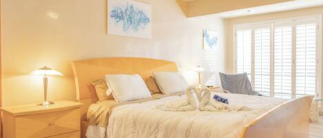 A hotel room with a large bed, two bedside tables, a nightstand, and a window with blinds.