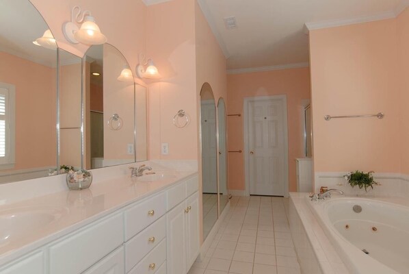 A bathroom with a large mirror, two sinks, a bathtub, and a door leading to another room.