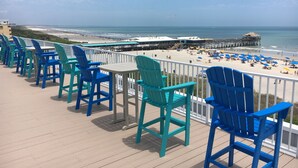 Une terrasse avec des chaises donnant sur une plage et une jetée.