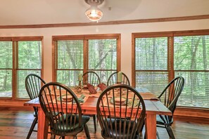 A dining area with a wooden table and chairs, large windows with blinds, and a ceiling fan. - Waterfront West Point Lake Cabin w/ Private Dock! (LaGrange)