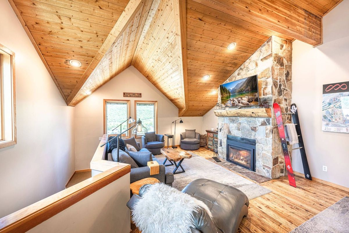Un salon chaleureux avec une cheminée en pierre, un plafond en bois et un téléviseur fixé au mur.