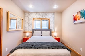A bedroom with a bed, two bedside tables, a window, and a wall-mounted artwork.