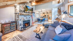 A cozy living room with a stone fireplace, a dining area, and a staircase leading to another level. - Old Town Ski House, Walk to Park City Mountain, Private Hot Tub, AC (Park City)