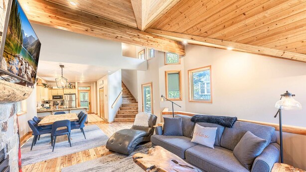 A modern living room with a wooden ceiling, a grey sofa, a coffee table, and a dining area with a wooden table and chairs. - Old Town Ski House, Walk to Park City Mountain, Private Hot Tub, AC (Park City)
