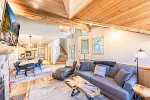 Un salon moderne avec un plafond en bois, un canapé gris, une table basse et un coin repas comprenant une table et des chaises en bois.